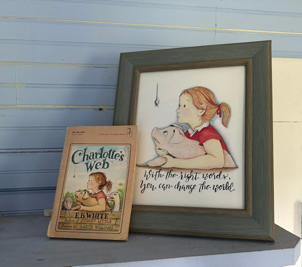 A copy of Charlotte's Web sitting on a shelf, in front of a framed picture of the book's main image.